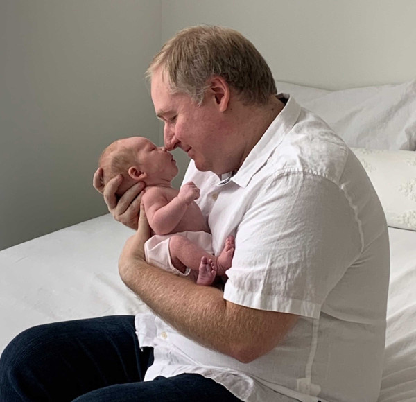 William holding his baby while sitting on a bed
